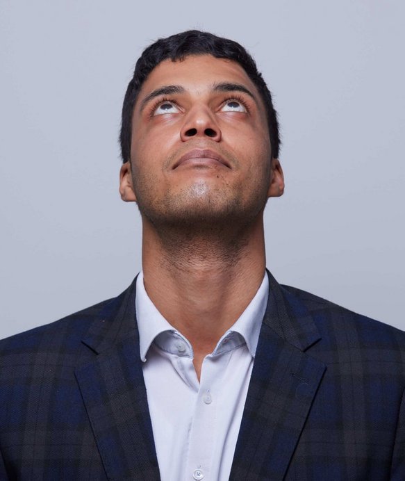 Ein Mann in einem karierten Anzug schaut nach oben, mit leicht geneigtem Kopf. Der Hintergrund ist einfarbig grau.