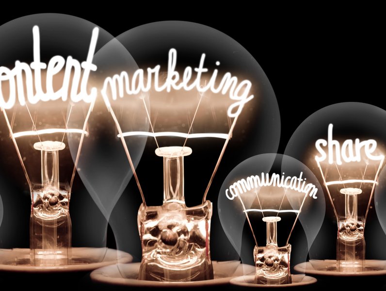 Glühbirnen zeigen leuchtende Wörter „content“, „marketing“, „communication“ und „share“ in geschwungener Schrift auf schwarzem Hintergrund. Die Wörter sind Teil der Glühfäden und stehen für Ideen und Austausch.