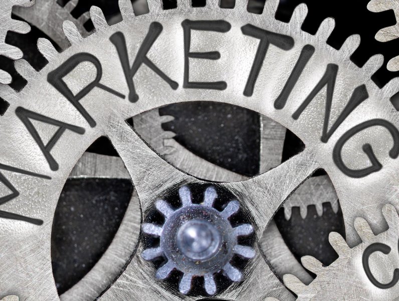 Ein großes Zahnrad mit dem Wort "MARKETING" greift in kleinere Zahnräder. Diese symbolisieren Zusammenarbeit und Mechanik als Konzept in einem industriellen Umfeld.