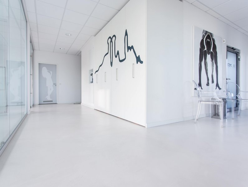 Minimalistischer Büroflur in Weiß mit abstrakter, schwarzer Wandkunst. Das klare Design und die Glaswand schaffen eine helle, inspirierende und moderne Arbeitsatmosphäre